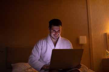 Man lying on bed at home and working with laptop late at night.