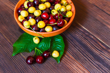 Yellow and red sweet cherry in a clay plate on a wooden background. Freshly picked sweet cherry