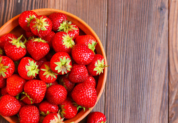 Red tasty strawberries in a clay plate on a wooden background. Freshly picked strawberries
