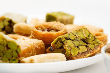 Traditional oriental sweets in white plate with different nuts on a white table, side view, close-up