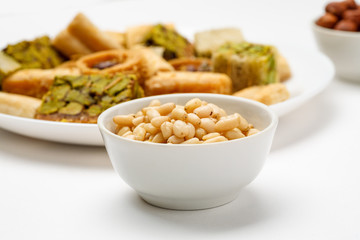Pine nut in ceramic bowl with traditional oriental sweets in the background, close-up