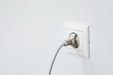 Electric outlet with plugged in wire on white wall