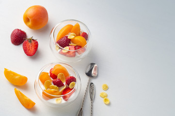 Light vitamin healthy dessert of sliced strawberry, apricot and cornflakes with cream in glass creamers