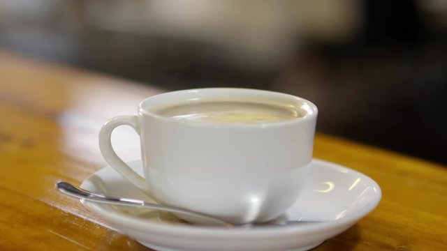 Cinemagraph of steaming cup of hot coffee standing on wooden table