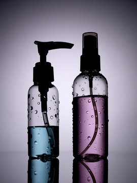 Plastic toiletry bottles with blue and purple liquid on a dark background