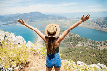 Happy woman with hands up standing on cliff over sea and islands at summer. Vintage mood, concepts of winner, freedom, happiness etc.