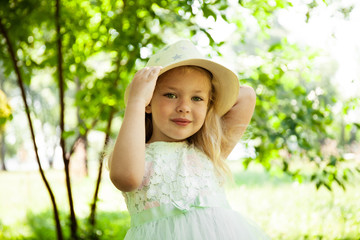 Portrait of cute child girl model in hat smiling in park or outdoor. Happy childhood, summer holidays and vacations.