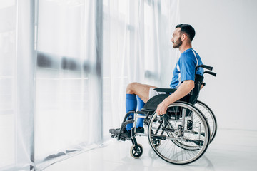 man in football uniform sitting in Wheelchair and looking through window