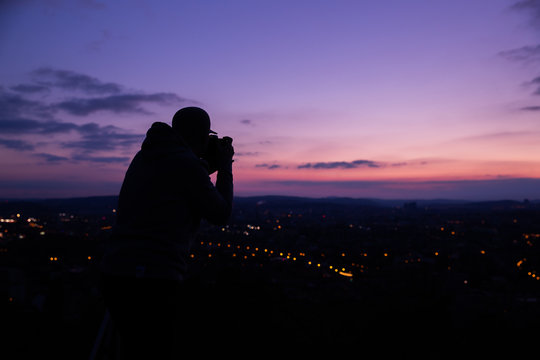 Photographer taking photos of colorful sunset on Bila Hora with amazing view on city Brno Czech Republic pink and orange colors with many clouds and city lights