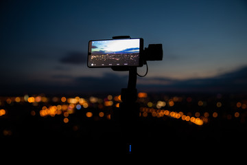 Fototapeta premium Mobile phone taking pictures on colorful sunset on Bila Hora with amazing view on city Brno Czech Republic pink and orange colors with many clouds and city lights