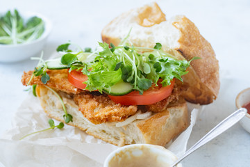 Sanwich with fried chicken on chiabatta with tomatoes, cheddar cheese, cucumber, onion, salad and microgreens