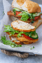 Sanwich with fried chicken on chiabatta with tomatoes, cheddar cheese, cucumber, onion, salad and microgreens