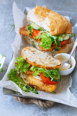 Sanwich with fried chicken on chiabatta with tomatoes, cheddar cheese, cucumber, onion, salad and microgreens