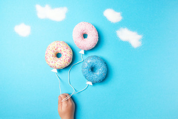 Colorful donuts on blue background, creative food minimalism, donuts in a shape of balloon in the sky with clouds made of sugar, top view
