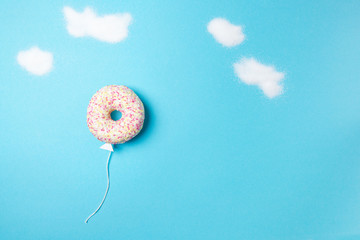Donut on blue background, creative food minimalism, donut in a shape of balloon in the sky with clouds made of sugar, top view