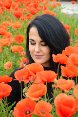 Naklejka premium Portrait of pretty woman in field of red poppy flowers, spring time