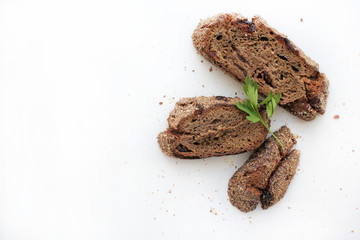 Pieces of homemade rye bread with cranberries and a sprig of parsley on a white background with free space for text.