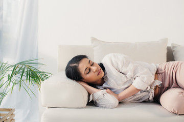 Obraz premium beautiful tired latin woman lying with closed eyes on sofa at home