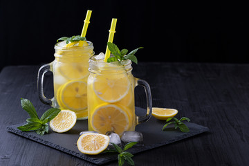 Lemonade in a jar with ice and mint on a black wooden table. - obrazy, fototapety, plakaty