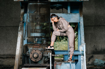 Fototapeta na wymiar Beautiful young stylish girl posing at abandoned factory outdoor with an old broken engine.