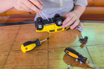 repair child yellow typewriter boy's hands hold a screwdriver and unscrew the screw twin screwdrivers and bolts lie on the table