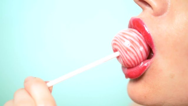 close-up, female sexy lips with red lipstick suck big pink round lollipop. copy space. blue background