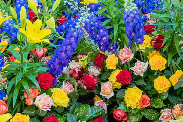 Strauß mit gelben, roten und weiß rosa farbenen Rosen mit blauem Rittersporn und gelben Lilien