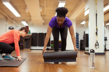 Fototapeta premium Female athletes placing exercise mats on hardwood floor in yoga class