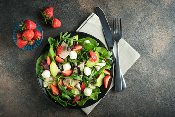 Salad with fresh strawberries, arugula, basil, avocado and mozzarella on a dark background top view copy space.