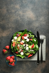 Salad with fresh strawberries, arugula, basil, avocado and mozzarella on a dark background top view copy space.