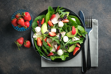 Salad with fresh strawberries, arugula, basil, avocado and mozzarella on a dark background.