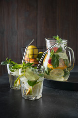 Detox lemonade with lime, orange, lemon, strawberry in glass and jar. Summer healthy freshness drink. Dark wooden background.