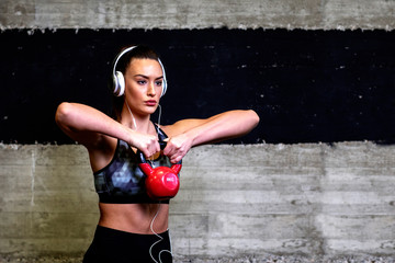 Strong woman exercise in gym with weight while listening music over headphones