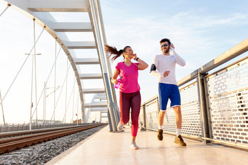 Obraz premium Couple exercise on the bridge at the end of day with headphones on head