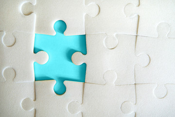 Multiple white puzzle pieces put together without one piece. View from above. Close up image.