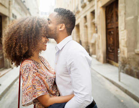 Side view of loving boyfriend kissing on girlfriend's forehead while standing in city