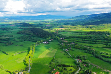 Aerial perspective view on sudety mountains during cloudy day with villages in the valley surrounded by meadows, forest and rapeseed fields