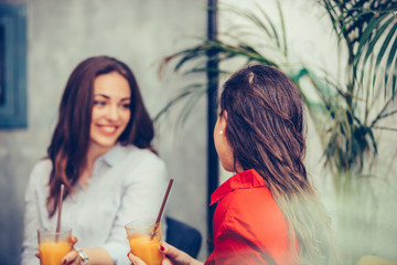 Two happy young women talking and drinking fresh fruit juice in a cafe