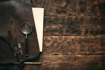 Leather bag and a blank letter with a pen a magnifying glass on brown desk flat lay background with copy space.