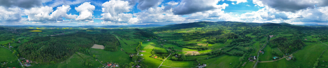 Aerial wide panoramic view on sudety mountains with touristic city in the valley surrounded by meadows, forest and rapeseed fields.