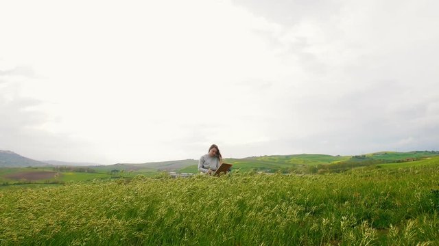 A young attractive woman sits in the middle of a green meadow