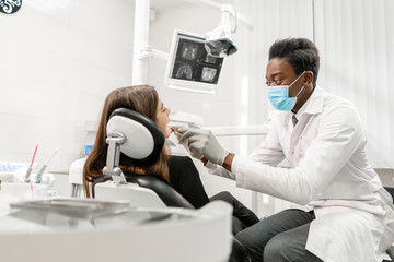 Fototapeta na wymiar Doctor treats teeth. Young African male dentist with a patient. Woman in the dentist chair at dental clinic. Medicine, health, stomatology concept. dentist treating a patient.