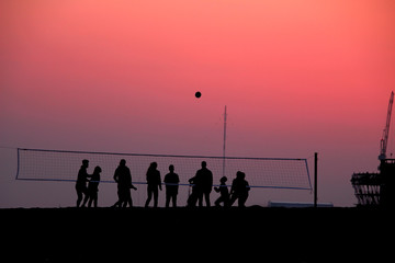 Fototapeta na wymiar silhouettes of people playing beach volleyball at sunset by the sea