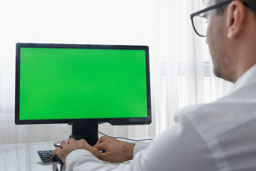 Engineer, Constructor, Designer in Glasses Working on a Personal Computer with a Green Screen on Monitor which has Chroma Key Great for Mockup Template. Using Smartphone or Tablet with Blue Screen