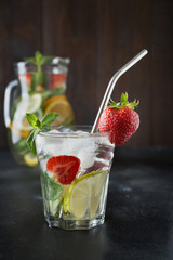 Detox lemonade with lime, orange, lemon, strawberry in glass and jug. Summer healthy freshness drink. Dark wooden background.