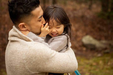 Fototapeta premium Side view of loving father kissing cute happy daughter while standing in forest