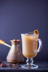 Copper coffee pot (Cezve) and coffee beans. Coffee with milk on dark background. Latte and black chocolate on slate board. Milk drink in glass beaker and dried rose
