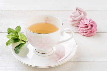 GREEN TEA WITH MINT AND MARSHMALLOWS ON WHITE WOODEN BACKGROUND