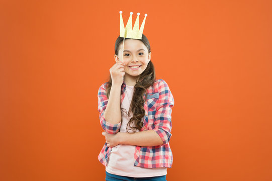 Prop, to make it really fun. Happy girl wearing crown photobooth prop on orange background. Happy little child holding crown prop on stick. Small princess smiling with fancy party prop