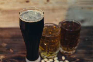 two mugs of light beer and a glass of dark beer on a wooden background